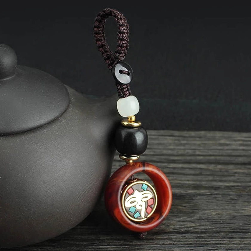 Side view of rotatable Buddhist keychain with unique rotating golden emblem on wooden table with teapot and spiritual decor