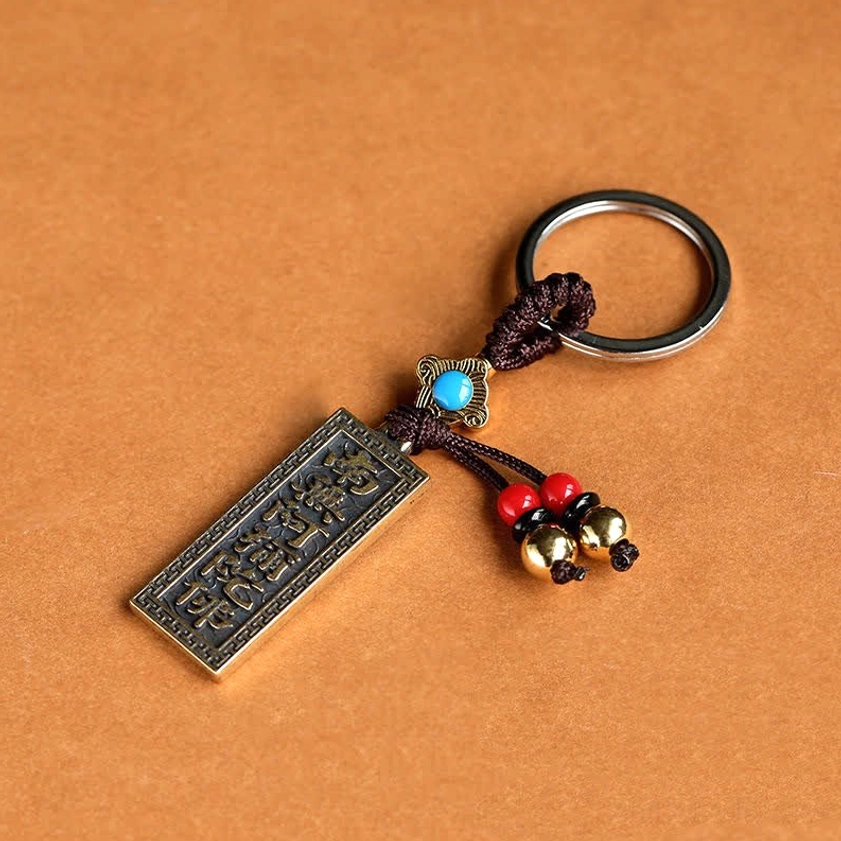Flat lay view of Buddhist blessing keychain with reversed sutra text tag and blue bead decoration on orange background