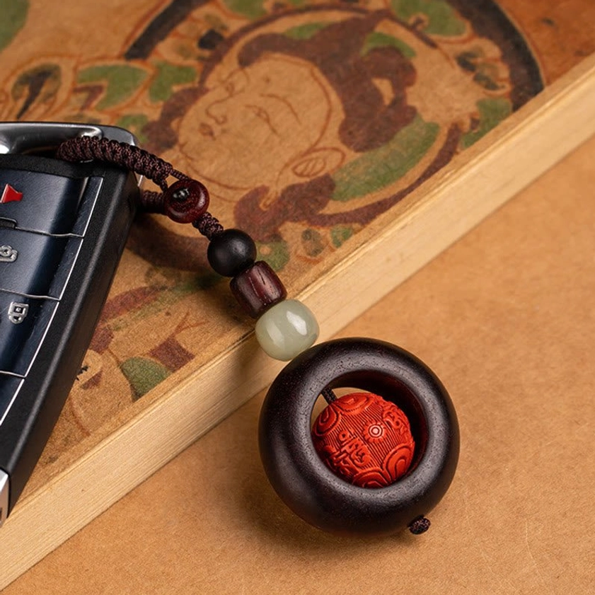 Buddhist keychain attached to car remote key fob, showing practical everyday carry application on vintage patterned background