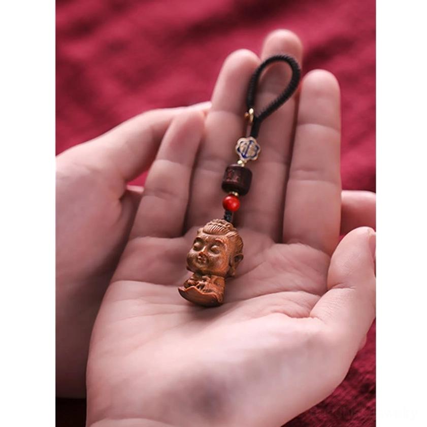 Buddhist keychain with green sandalwood Buddha pendant shown in overhead view on red fabric background