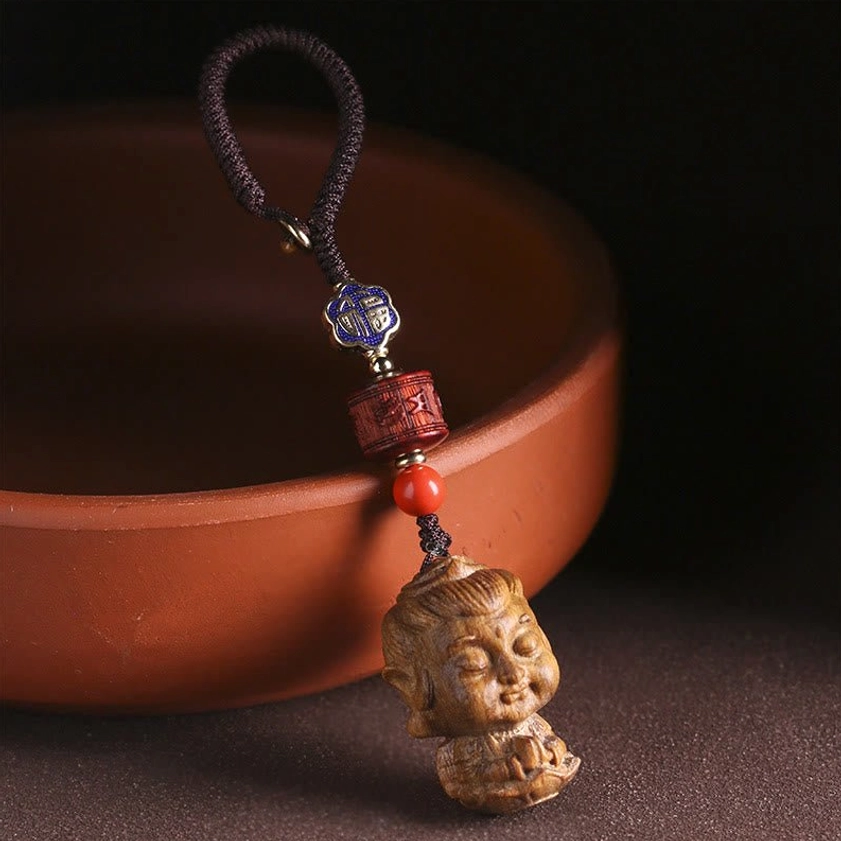 Buddhist keychain pendant hanging showing green sandalwood Buddha head with woven cord and warm earth tone beads