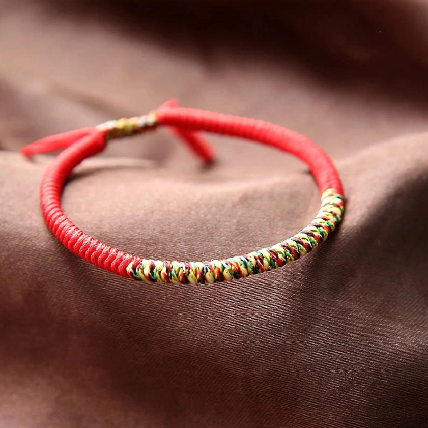 Bright red Buddhist King Kong Knot bracelet with multicolor woven middle section and hand-woven adjustable tassel rope on brown satin background