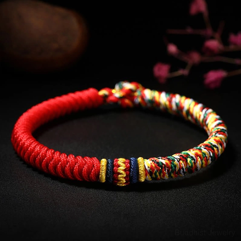 Handmade Buddhist King Kong Knot multicolored braided string bracelet with red base and vibrant colored accents, displayed on dark backdrop with floral decorations