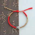 Handmade Buddhist King Kong knot red string bracelet with colorful woven threads and silver Buddha charm on calligraphy background
