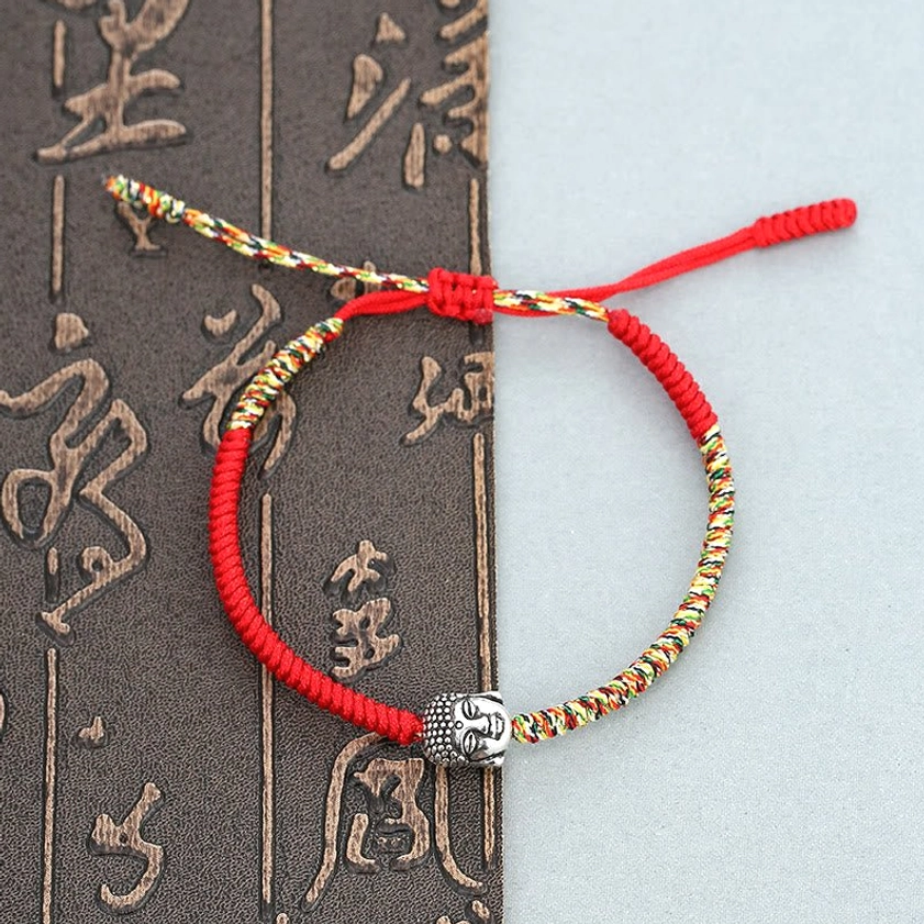 Handmade Buddhist King Kong knot red string bracelet with colorful woven threads and silver Buddha charm on calligraphy background
