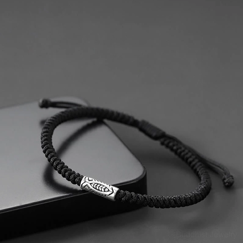 Adjustable black koi fish bracelet with sliding knot displayed on dark grey rectangular prop showing weave quality