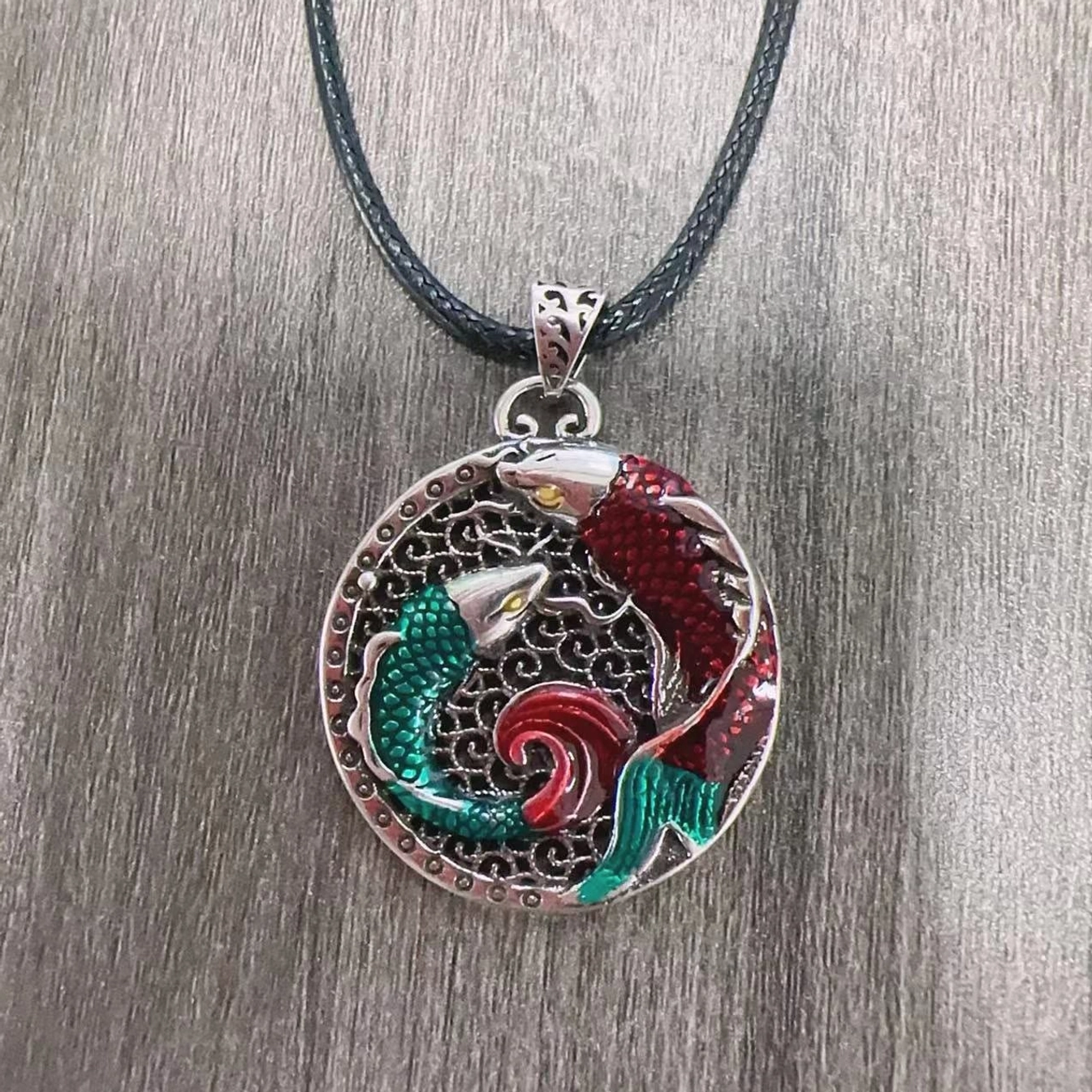 Handcrafted koi fish necklace with black leather cord and vintage silver copper pendant on wood texture background