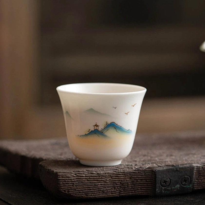 Handcrafted Buddhist mountain landscape ceramic tea cup with white porcelain body and traditional hand-painted artwork, low angle view on weathered wood