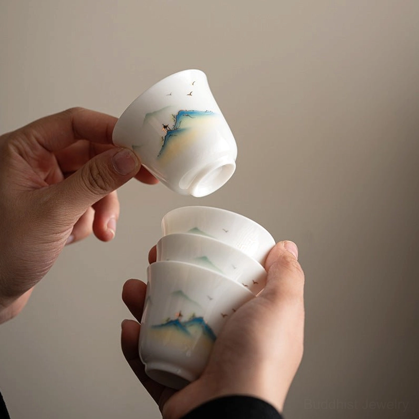 Stack of handcrafted Buddhist landscape ceramic tea cups with matching hand-painted designs, top-down view on light background