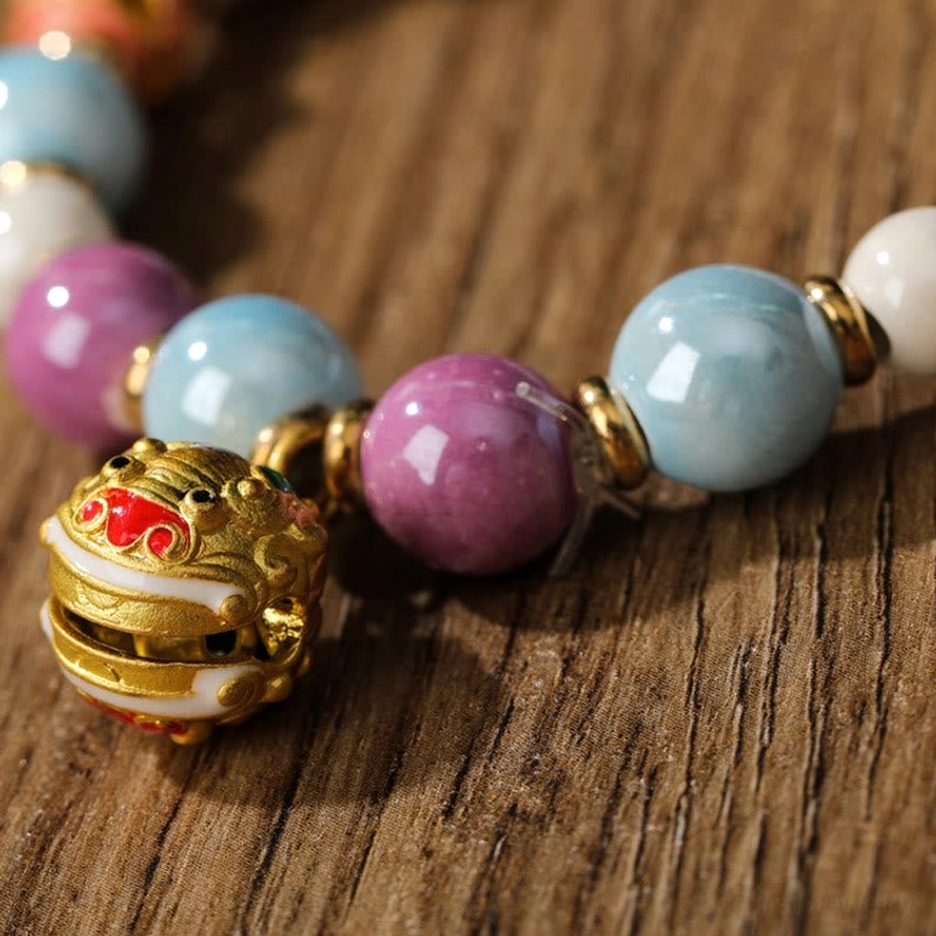 Macro close-up of Buddhist bracelet charm and bead details featuring lion head enamel pendant and gold metal spacer rings