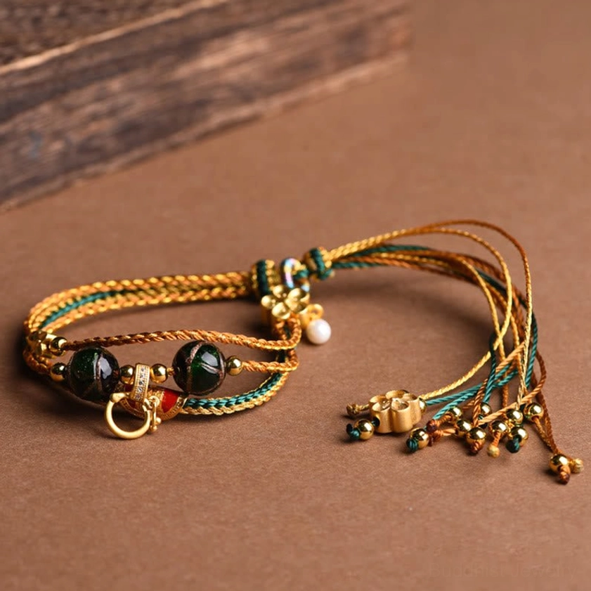 Buddhist protection bracelet with dark green glass beads, red enamel metal accents, and tassel pendants on wooden background