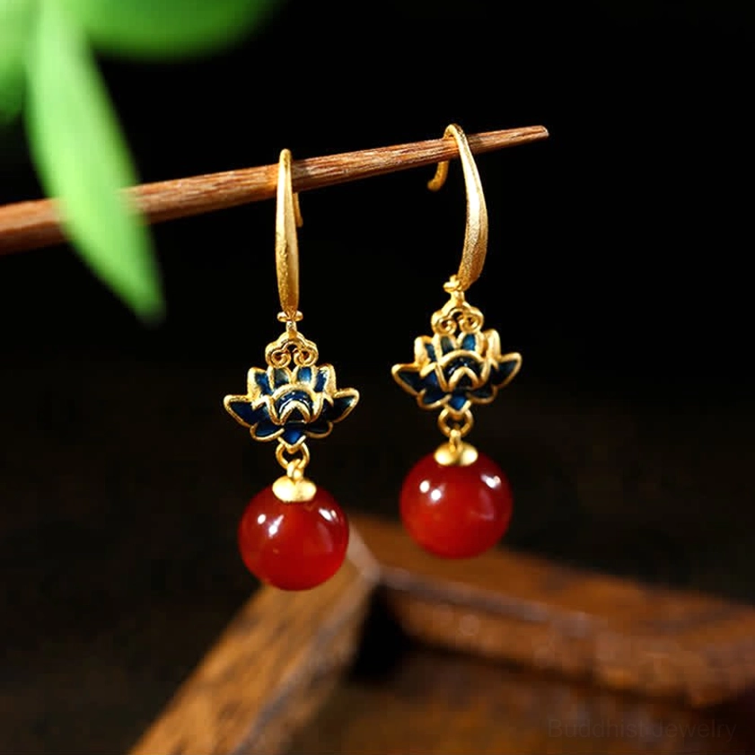 Handcrafted red agate and lotus enamel earrings hanging from wooden branch with green foliage, showcasing glossy stone beads and gold hooks