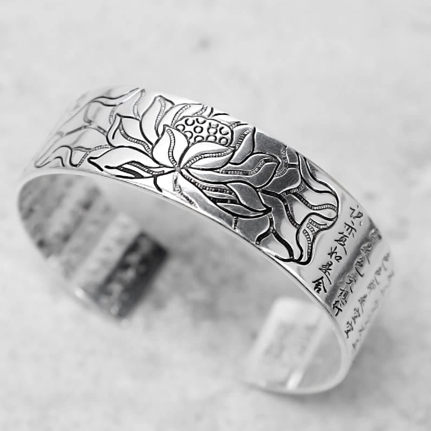 White copper lotus cuff bracelet high side angle view displaying relief engraving and horizontal Buddhist scriptures on silver-toned finish
