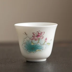 Handcrafted Buddhist ceramic tea cup featuring pink lotus flower and lotus leaf design with dragonfly motif, displayed on dark wooden table