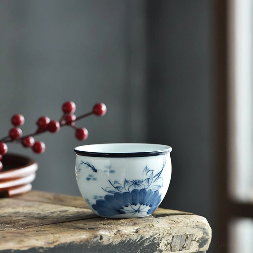 Single blue and white ceramic tea cup featuring prominent lotus bloom pattern with dark blue rim, front view