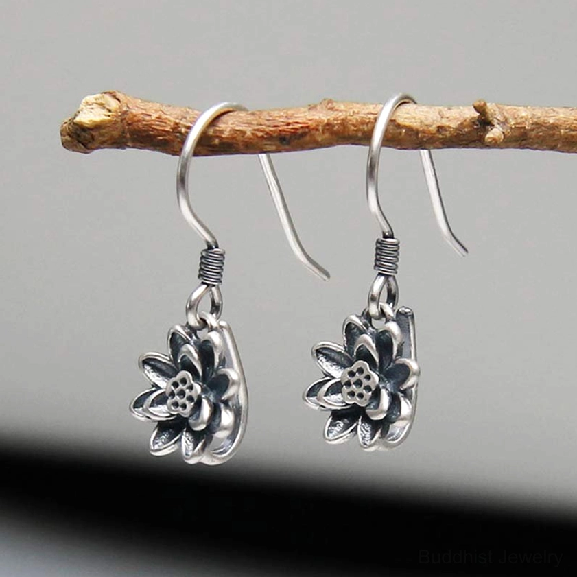 Antique silver lotus dangle earrings with embossed lotus texture, front low angle on wooden twig