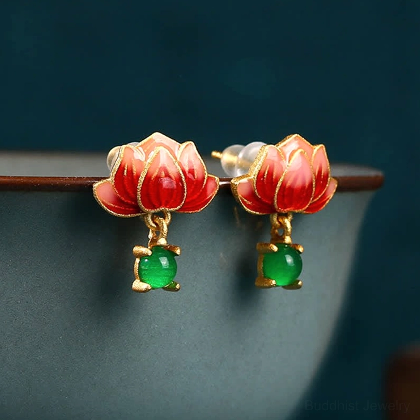 Front view of Buddhist lotus earrings pair with gradient red enamel and gold hardware, resting on ceramic bowl edge, showcasing detailed lotus flower design