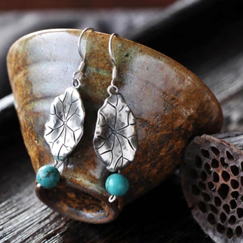 Lotus leaf silver earrings with turquoise bead accents displayed with teacup and lotus pod