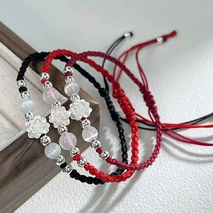 Multiple Buddhist protection string bracelets with silver lotus charms and cat's eye beads on wooden tray
