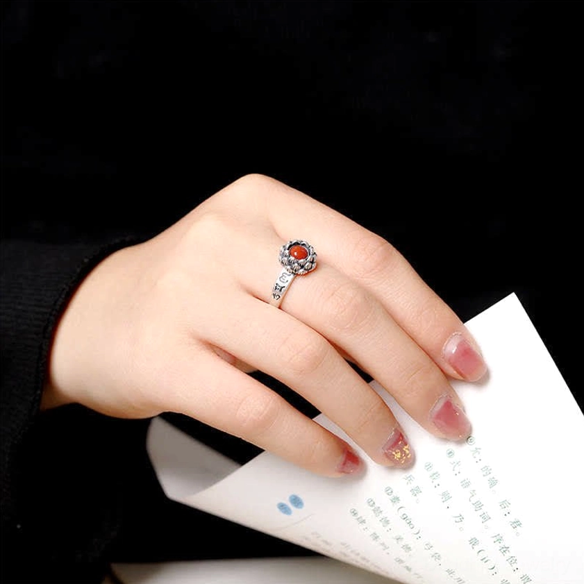 Hand wearing sterling silver lotus red agate ring on middle finger in indoor reading setting