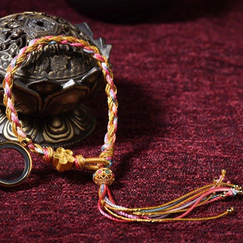 Handmade Buddhist lucky string bracelet close-up showing braided multicolor threads, gold flower decoration and metal ring with tassel
