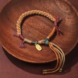 Handwoven Buddhist lucky bracelet with multicolor braided rope, golden Fu charm, and decorative tassels on wooden plate
