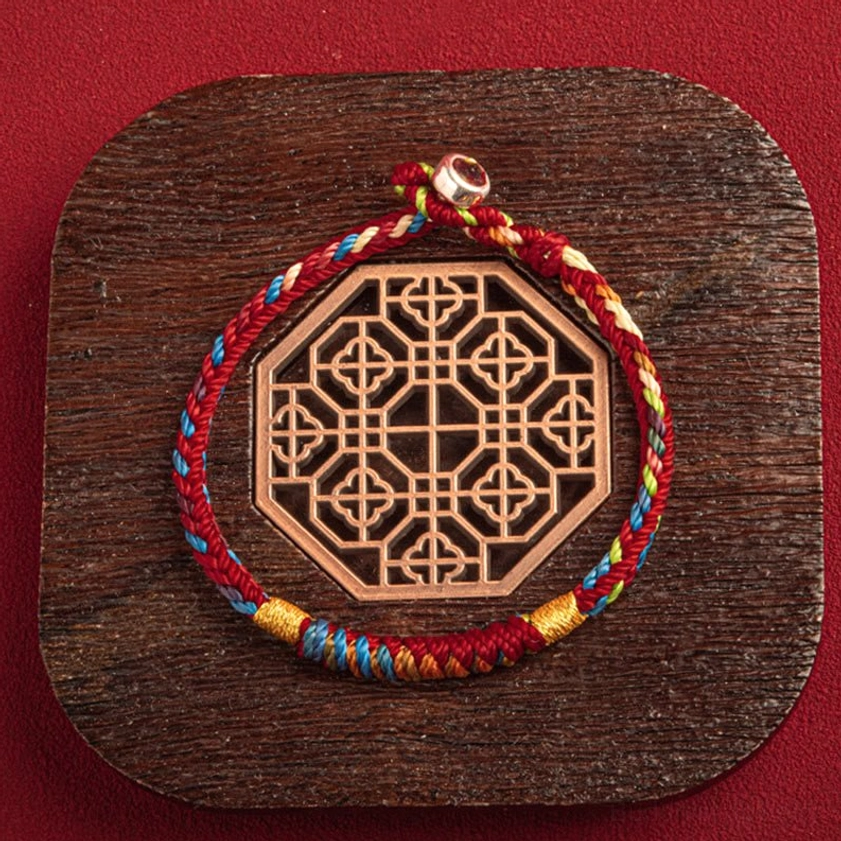 Top-down view of lucky multicolored Buddhist bracelet with King Kong Knot next to decorative wooden ornament
