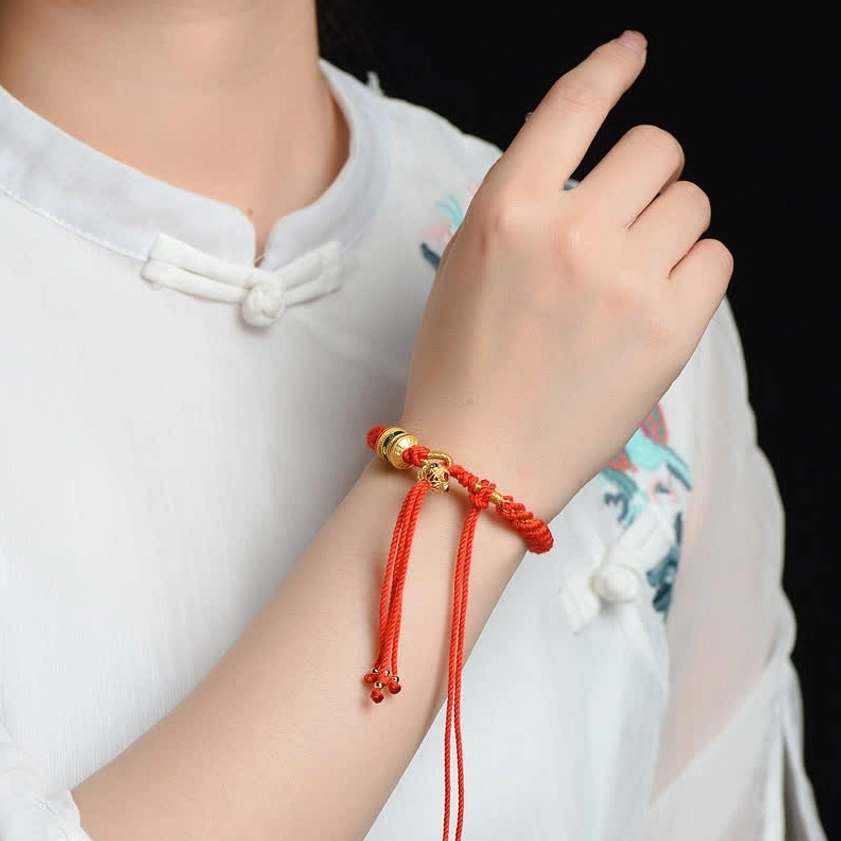 Buddhist prayer wheel bracelet worn on wrist, red woven cord with gold accents and floating tassel ends