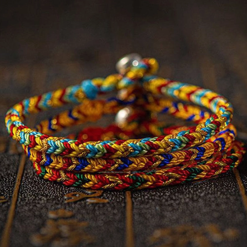 Stacked multicolored Buddhist bracelets close-up overhead view, displaying layered woven design with shiny silver metal beads on dark sacred background