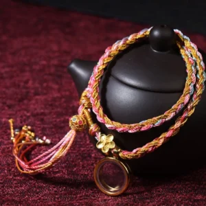 Handmade Buddhist lucky braided string bracelet with multicolor threads, metal flower charm and tassel - main product view on dark red cloth