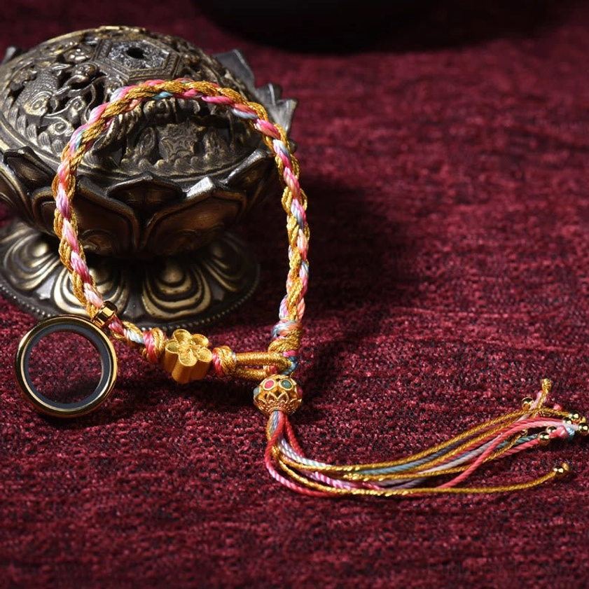 Single wrap Buddhist lucky braided string bracelet with multicolor threads, metal pendant and tassel ends on dark background