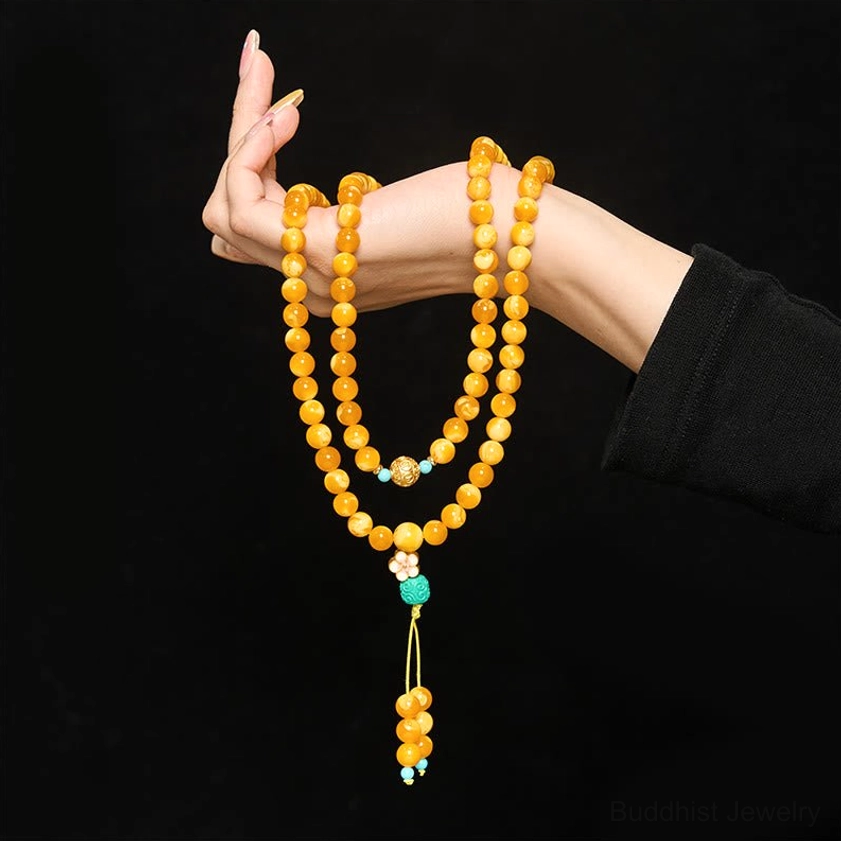 Delicate amber Buddhist mala prayer beads close-up, hand-held at eye level featuring metal spacer beads and turquoise pendant tassel