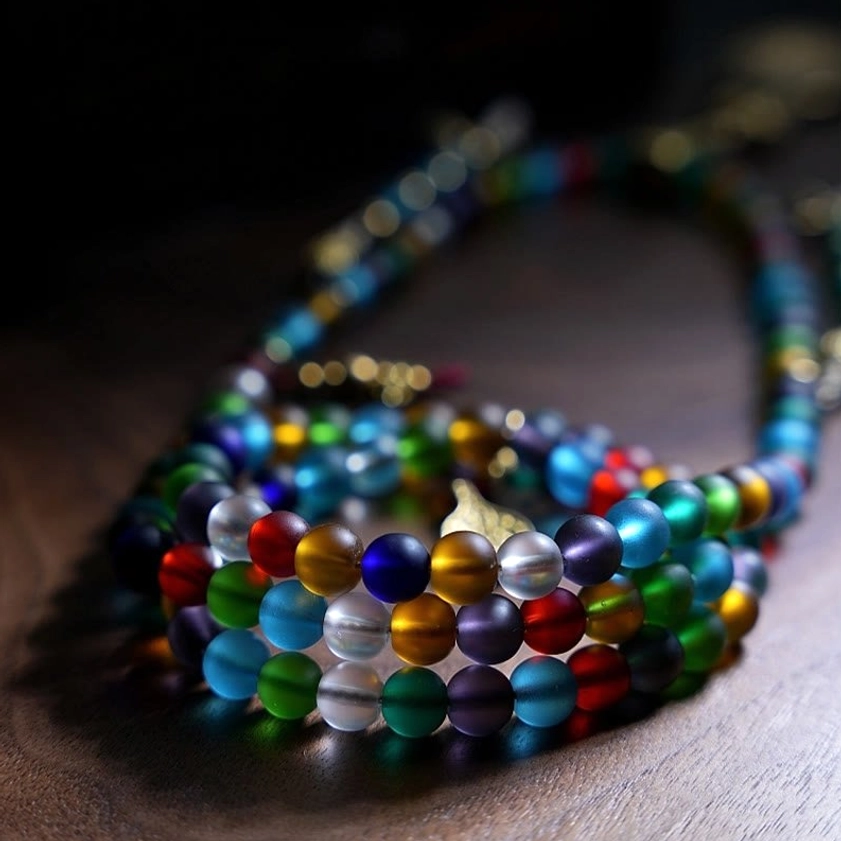 Coiled Buddhist prayer mala beads in vibrant mixed colors, close-up overhead view showing matte Liuli glass finish and metal prayer bead counters