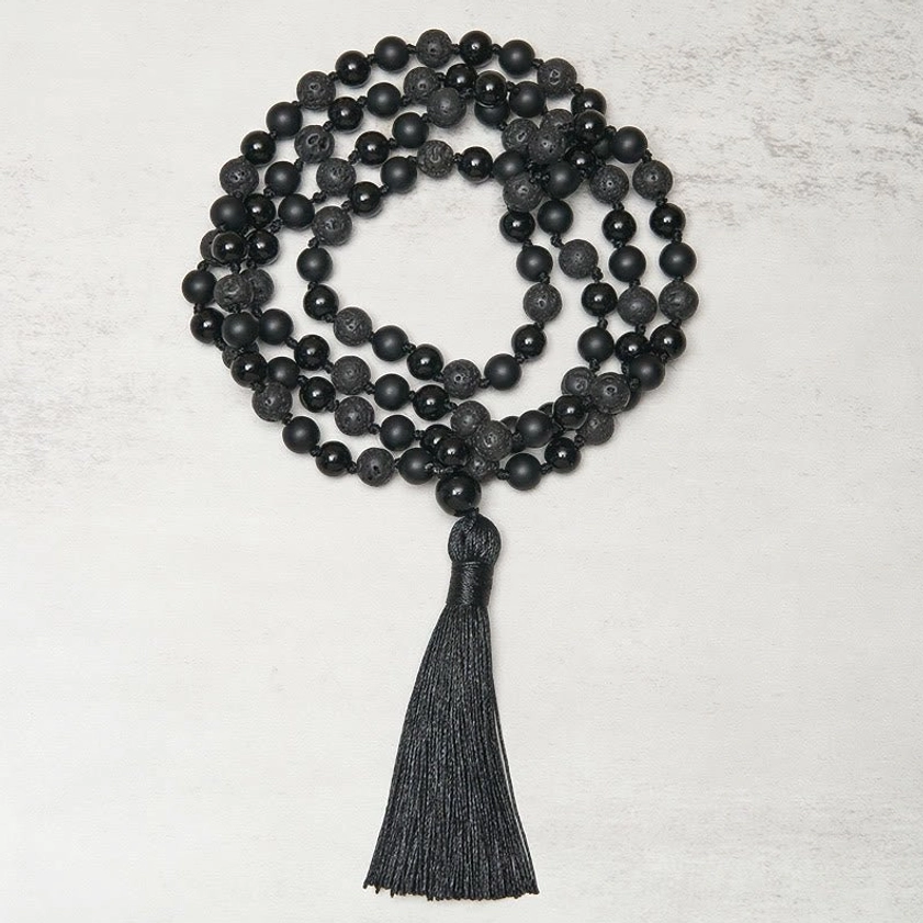 Coiled Buddhist prayer mala with black gemstone beads and long decorative tassel, center flat lay photography