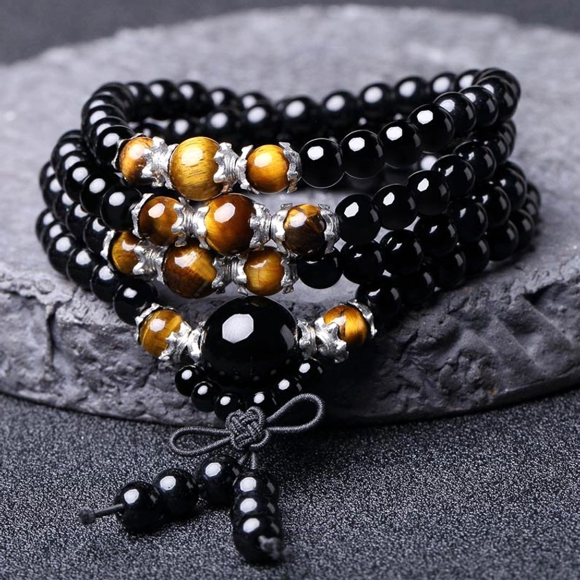 Close-up flat lay of 108 bead Buddhist mala featuring glossy black obsidian beads with golden tiger eye stone accents and knotted tassel