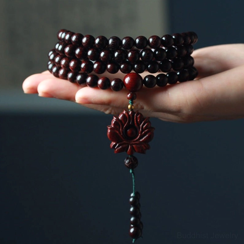 Red sandalwood mala bracelet held in palm showing deep reddish-brown beads large accent bead and lotus pendant with tassel