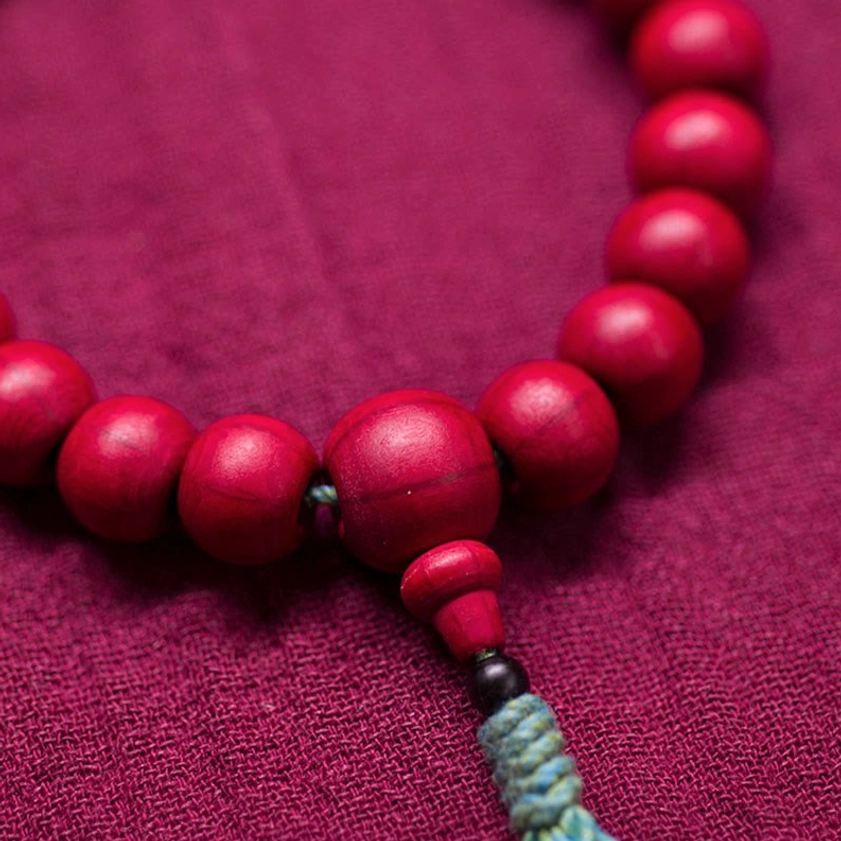 Buddhist wooden prayer mala bracelet side view showing crimson beads with woven teal tassel