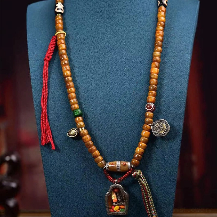 Full display of Buddhist mala necklace in jewelry stand studio setting featuring tan bone beads, red silk tie, metal charms, shrine pendant, and complete spiritual composition