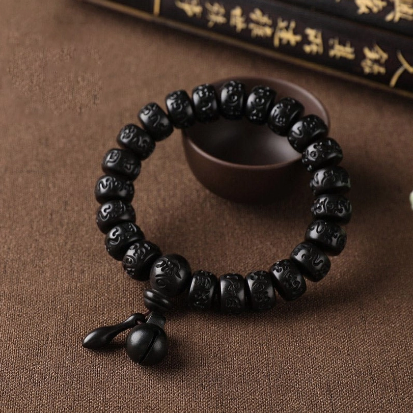 Double-layer Buddhist wooden mala bracelet with dual bell charms, carved mantra beads, and wooden bowl on brown fabric