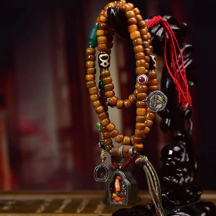 Tibetan Buddhist prayer mala necklace displayed hanging with three-quarter view showing tan cylinder bone beads, protective dzi stones, and red silk cord accents against dark backdrop