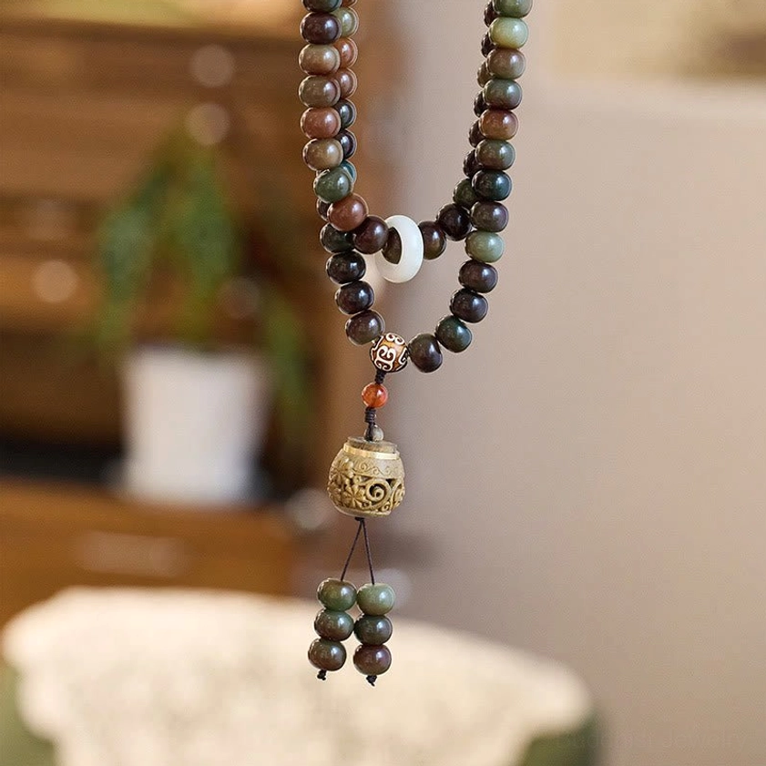 Buddhist prayer mala beads necklace photographed from low angle with white spacer bead, earthy tone beads, and carved wooden pendant