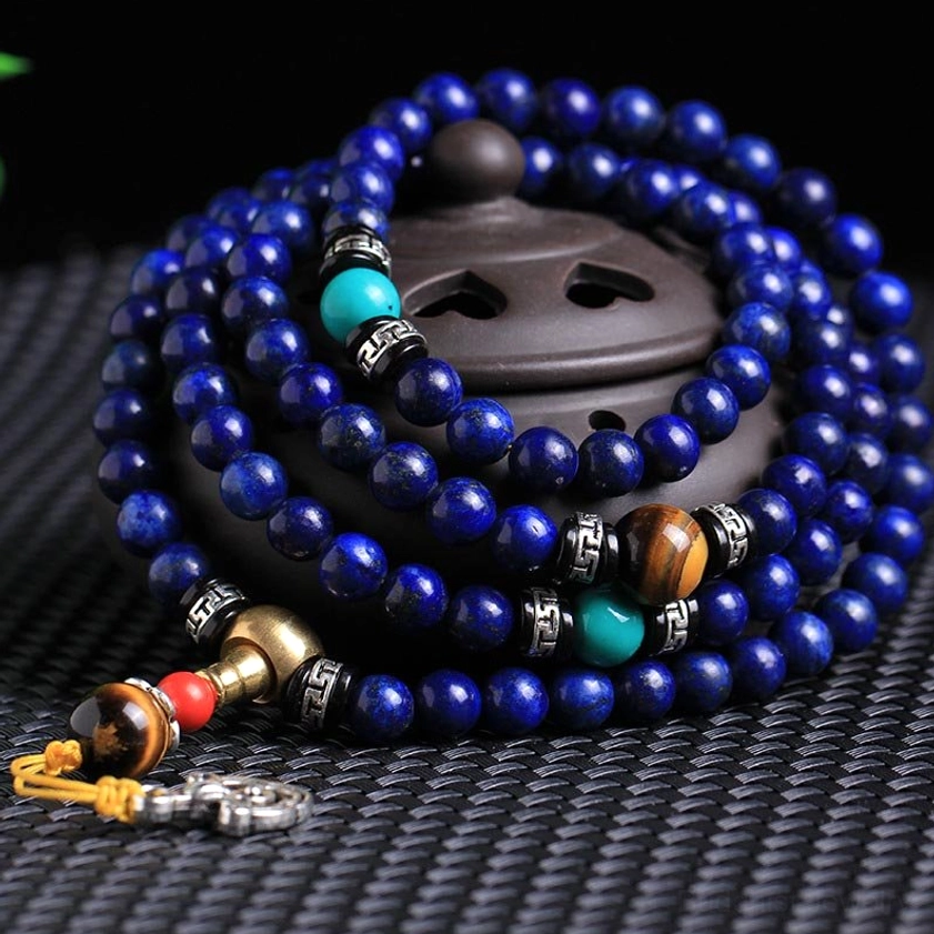 Close-up overhead view of lapis lazuli prayer mala set with blue beads turquoise tiger eye and silver hardware on wooden base
