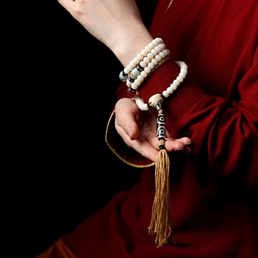 Worn Buddhist mala bracelets on hand with three-eye Dzi bead and cotton tassel pendant, layered spiritual practice
