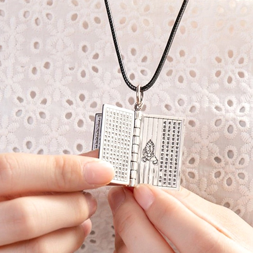 Hand holding open silver Buddhist sutra book pendant displaying full inner mantra text with flipable pages