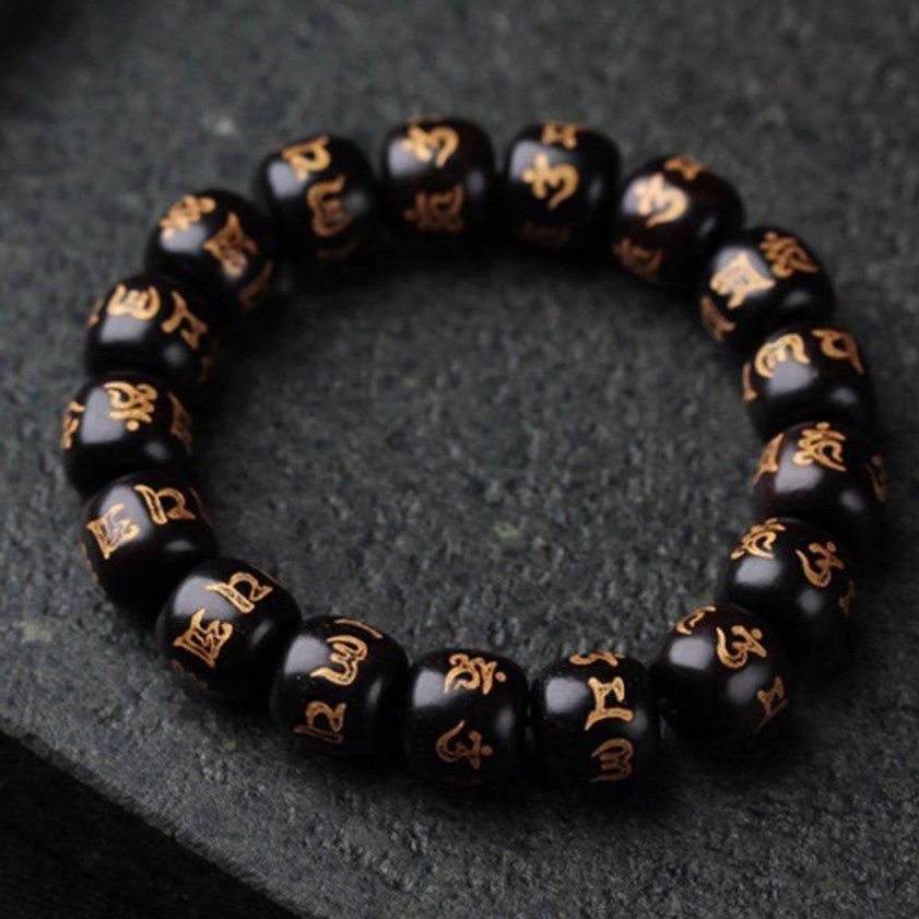 Buddhist prayer bead bracelet featuring six-syllable mantra gilded onto ebony beads, flat lay on dark stone surface