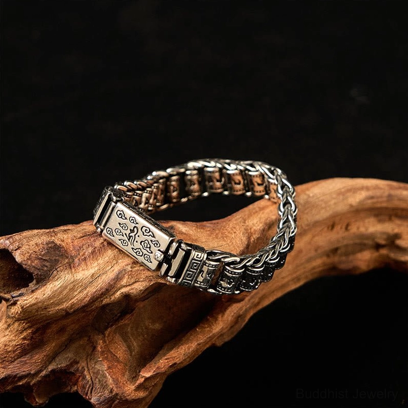 Three-quarter view of Buddhist mantra copper bracelet with carved clasp details and twisted chain links on wood branch