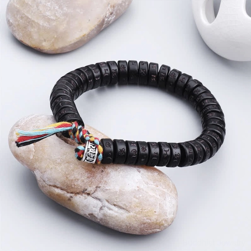 Buddhist mantra bracelet with black coconut shell beads and silver decorative accent, displayed with natural stone props