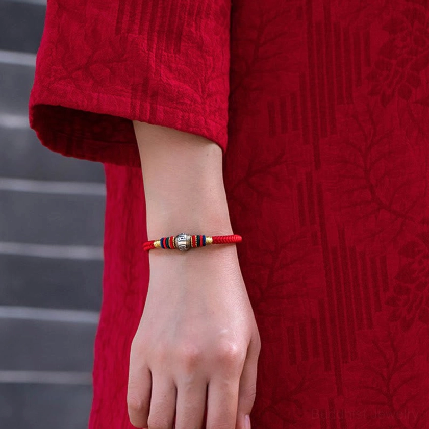 Close-up detail of red Buddhist braided bracelet with silver charm worn on wrist with red traditional clothing background