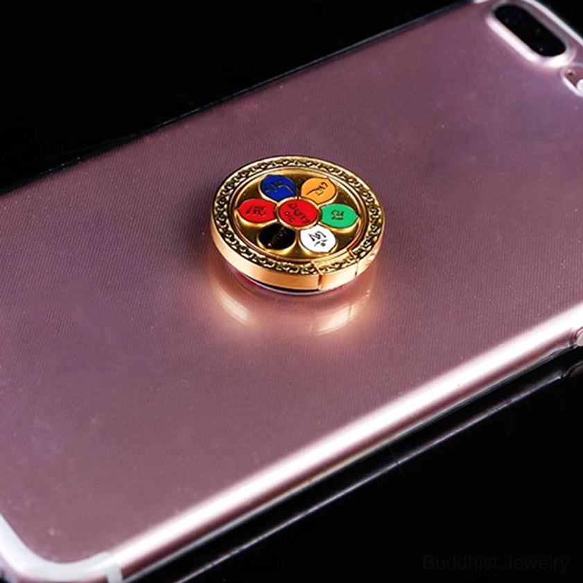 Close-up of Buddhist phone ring holder attached to pink smartphone back, gold-tone metal with multi-color enamel six-syllable design
