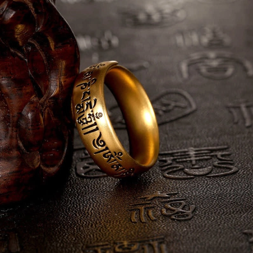 Six syllable Buddhist mantra ring showing open adjustable band with black Sanskrit text on antique gold tone, crafted leather display